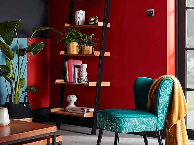 Green velvet chair with red wall with shelves and plants