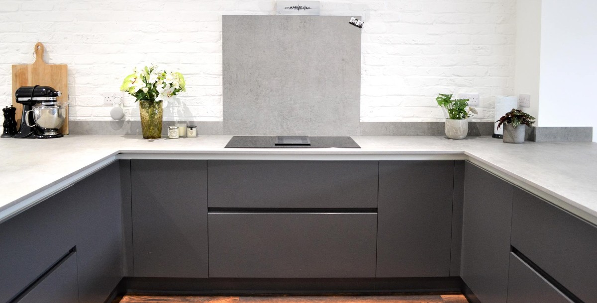 Small kitchen with white brick walls, dark blue handleless base units and a grey stone-effect splashback and worktop