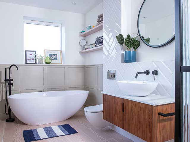 freestanding bath in panelled bathroom with basin and cupboard