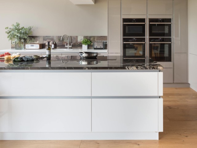 White handleless kitchen with a pale grey handle rail and dark marble worktop