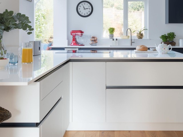 White contemporary handleless kitchen with a dark grey handle rail, white worktops and white walls
