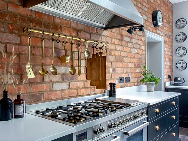 Range cooker with hob and golden utensils hanging in industrial style kitchen