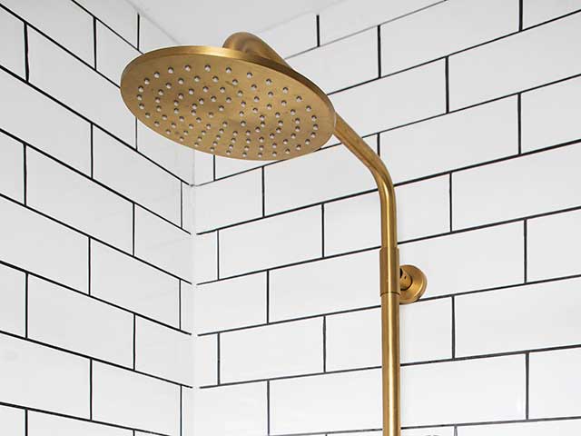 Gold fittings of shower with white tiles behind