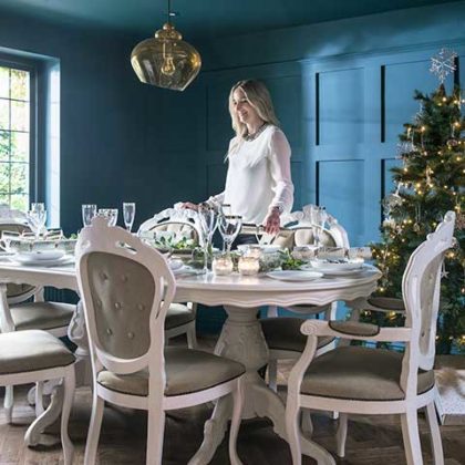 Christmas dinner table in a dining room with navy panelled walls, French-style dining table set and christmas tree