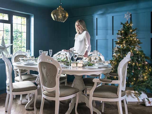 Christmas dinner table in a dining room with navy panelled walls, French-style dining table set and christmas tree