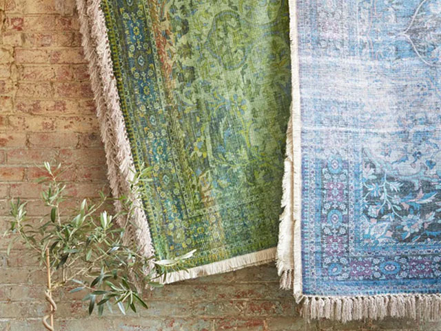 forest green colour rug hanging against a brick wall next to a blue rug