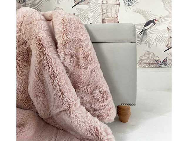 Pink faux fur throw over grey armchair with birdcage print wallpaper in background