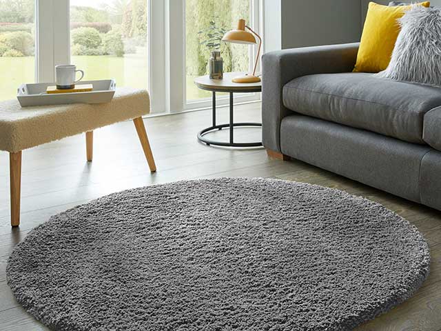 Circular grey fluffy rug from Dunelm Teddy range on wooden flooring with grey sofa and sheepskin stool in background
