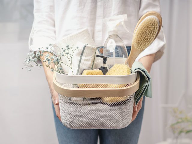 Woman holding cleaning basket full of sponges, brushes and cleaning sprays