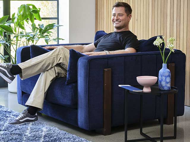 George Clarke Sofology collab relaxing on blue chair with panelled wall behind 