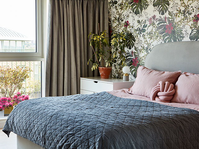 bedroom with bold floral wallpaper, blush pink bedding and blue/grey throw