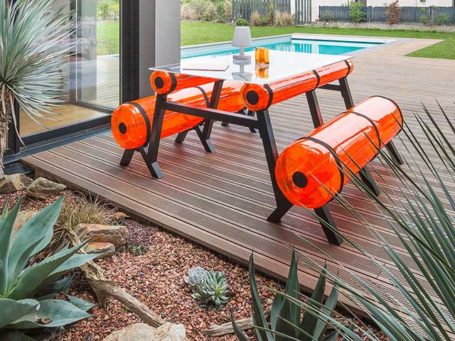 inflatable picnic bench in bright orange on decking with swimming pool behind