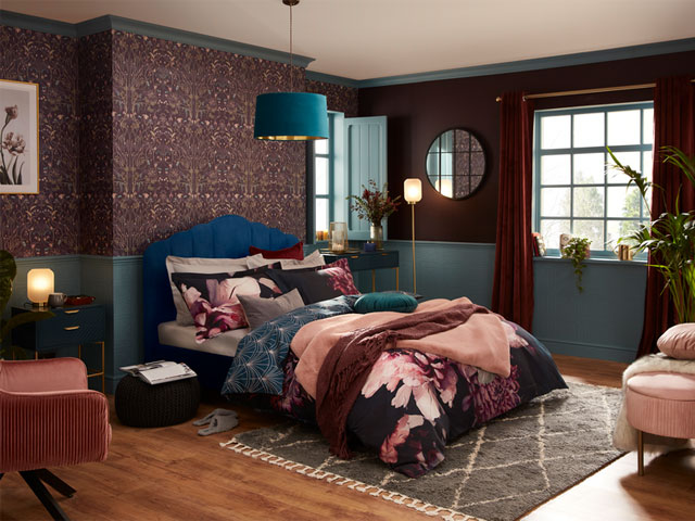 TikTok interior trends: maximalist bedroom with deep teal bed frame, burgundy bedsheets, scatter cushions and gold furnishings