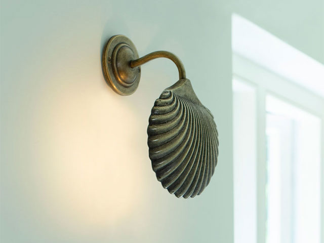 scallop-shaped wall light in aged brass on a pale green wall