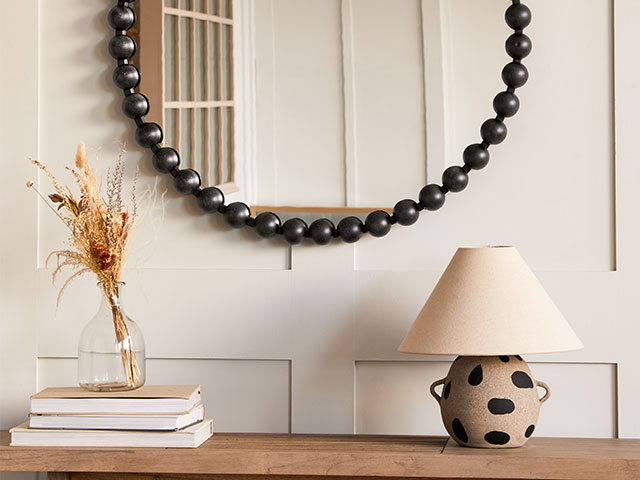 sideboard with ceramic lamp, dried flowers, artfully arranged books and bobbin-framed mirror