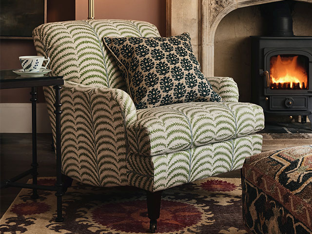 Cosy leaf-print armchair by the fire in an old cottage with original fireplace and wood burning stove