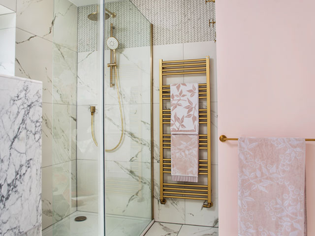 walk-in shower with marble-effect tiles, gold towel rail and pink walls