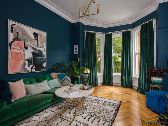 green velvet curtains in a living room with large bay window, green sofa and blue walls