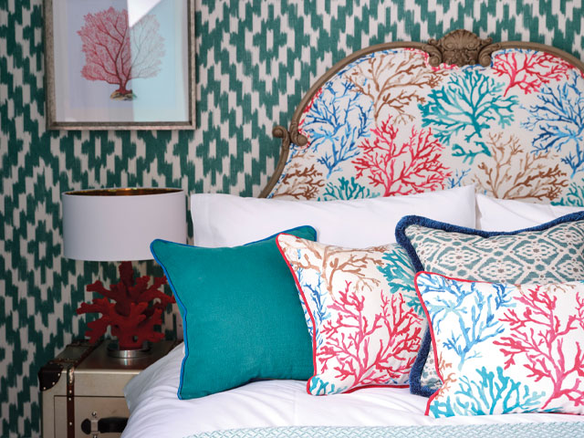 a bderoom in a fisherman's cottage with green printed wallpaper and pink cushions