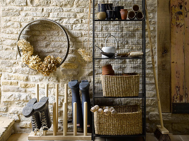 wooden welly rack and metal shelving stand with woven baskets against an exposed brick wall