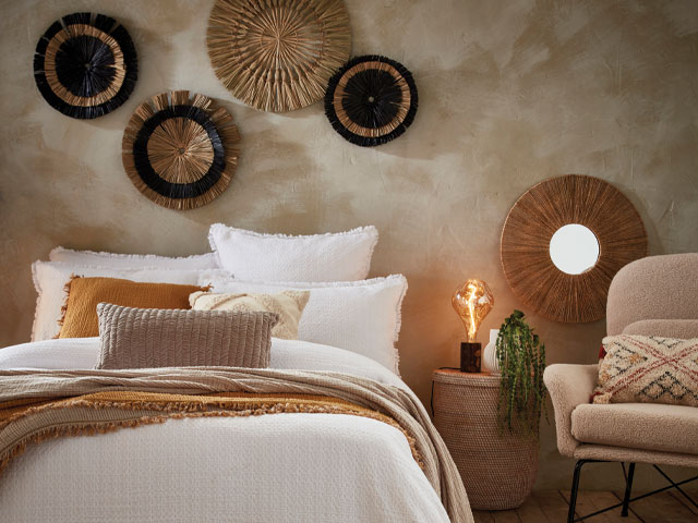 woven wall art on a clay plaster bedroom wall with lots of pillows, throws and texture