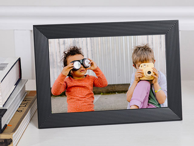 Digital photo frame showing a photo of a two young children playing with goggles and a camera