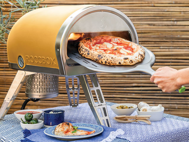 yellow pizza oven by Gozney on an outdoor table with a chef removing a cooked pizza