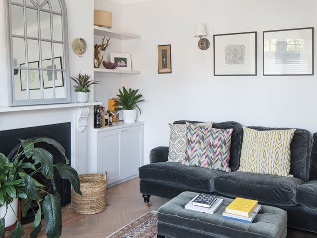 living room with inky blue sofa, alcove shelving, white walls and mirror above the fireplace