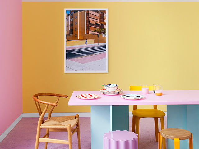 Yellow and pink dining room with wooden chairs and street view frame on wall