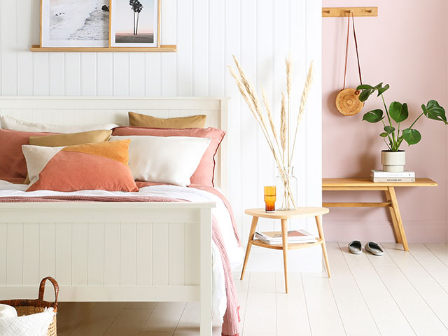 white wooden bed with pale pink and ochre cushions in a bedroom with pink walls and white wall panelling
