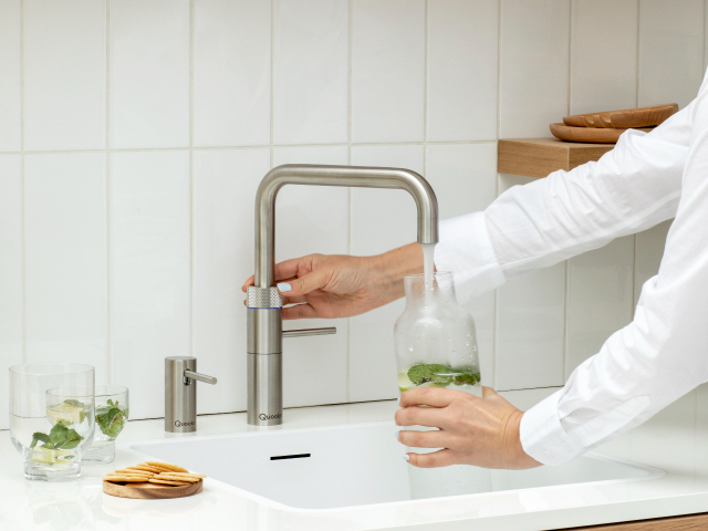 pouring instant chilled water from a chrome tap into a glass water jug with mint