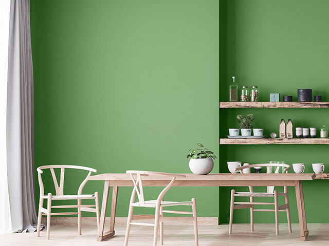 Summer green wall paint in dining room with wooden shelves, table and chairs