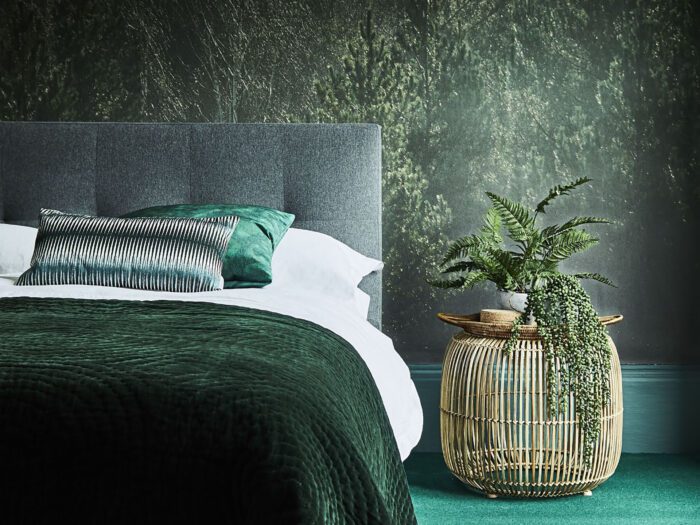 A bed with nature mural and wicker bedside cabinet