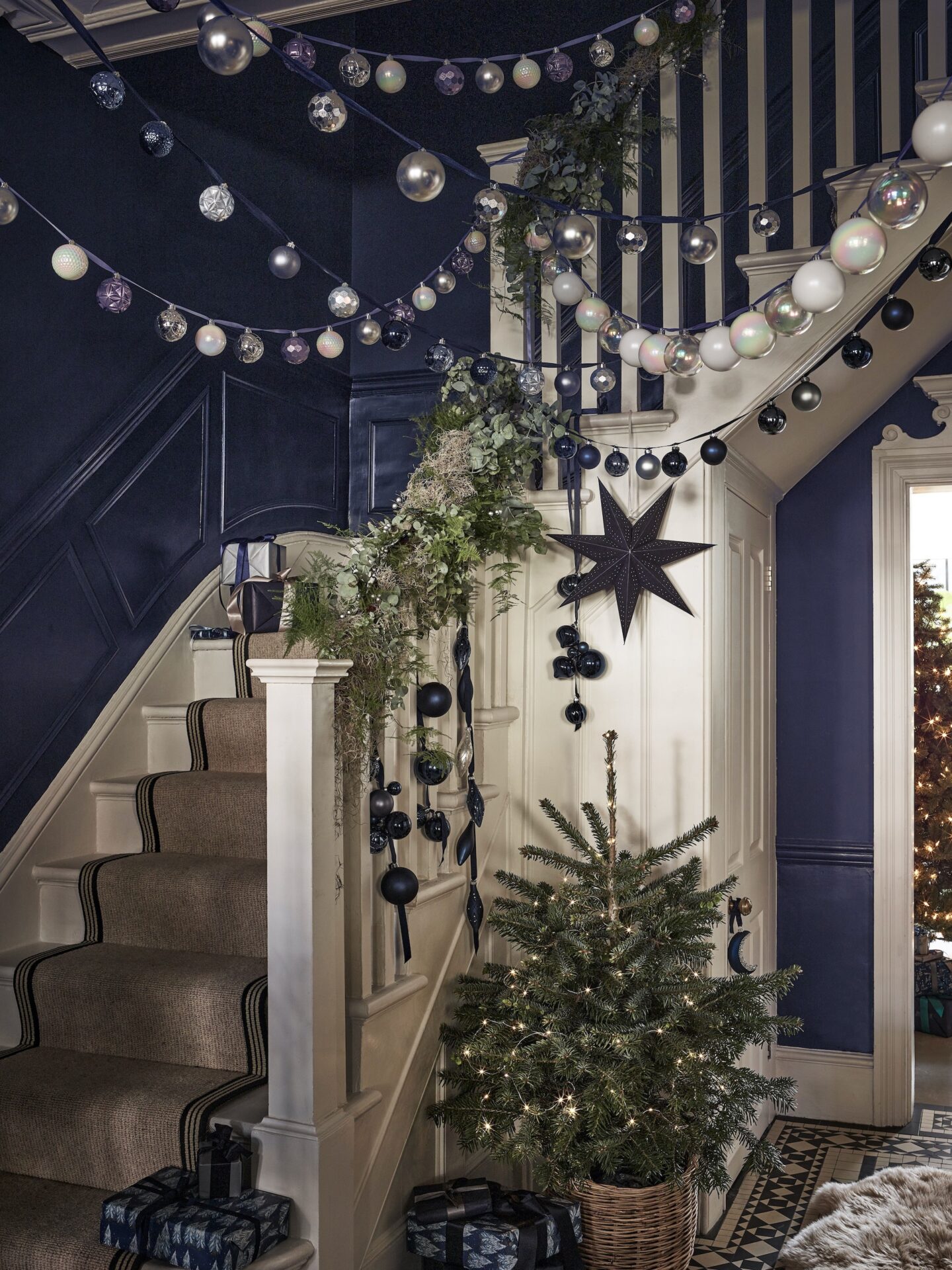Navy Christmas hallway with bauble garlands and a real tree.
