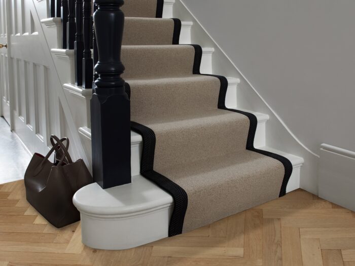 Beige stair carpet runner with black edging and white painted staircase