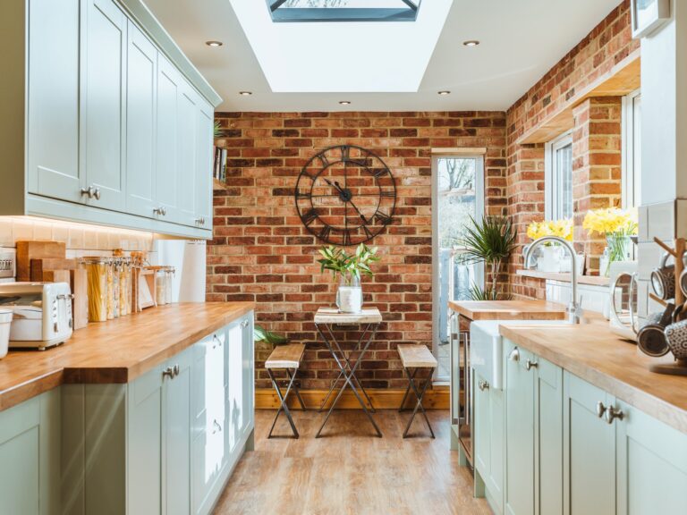 Sage green galley kitchen with exposed brick wall