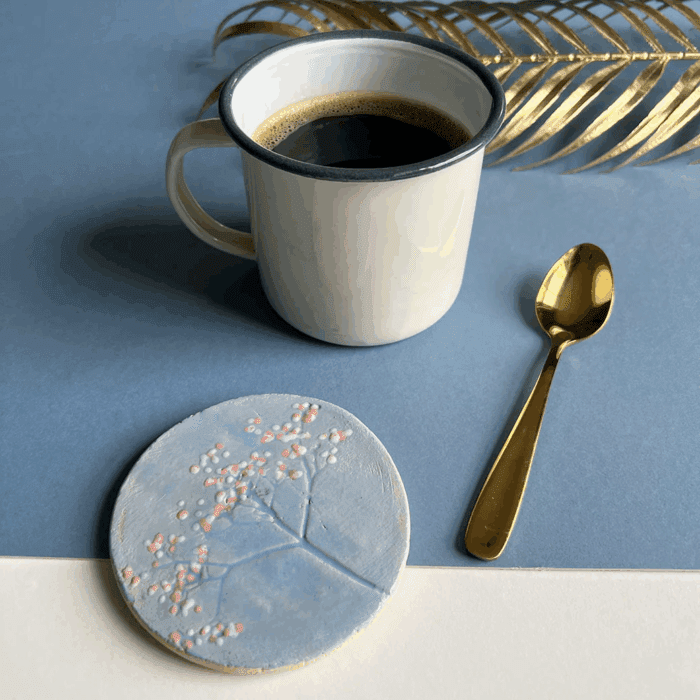 A decorated clay coaster next to a cup of coffee