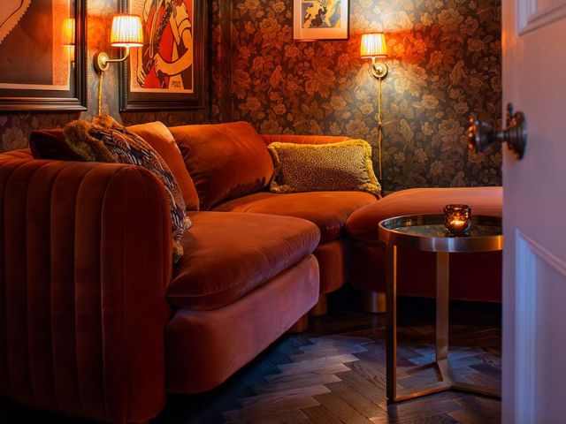 Red velvet sofa and dark wood flooring with ornate wallpaper